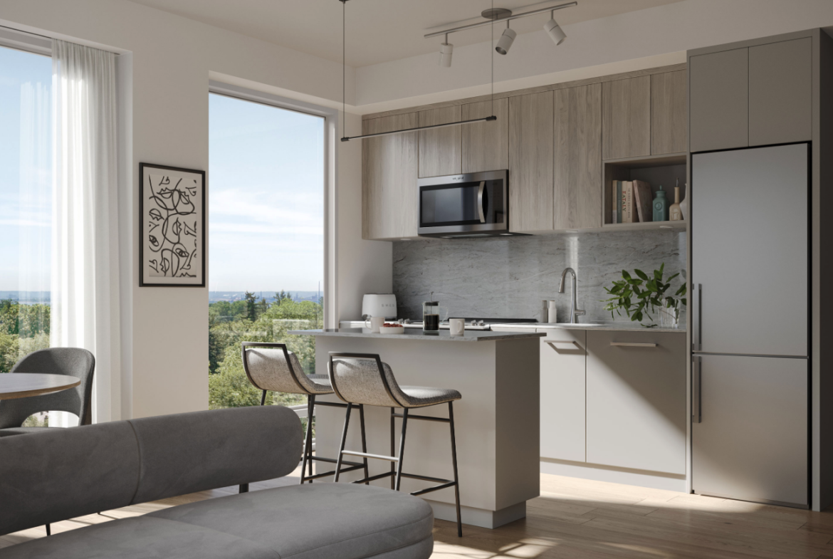 This modern kitchen interior features gray cabinets and a sleek island with barstools. A large window offers a view of greenery, while wall art and a potted plant add decorative touches. A micro-oven and stainless steel fridge complete the look, ideal for new homes with style-focused design.