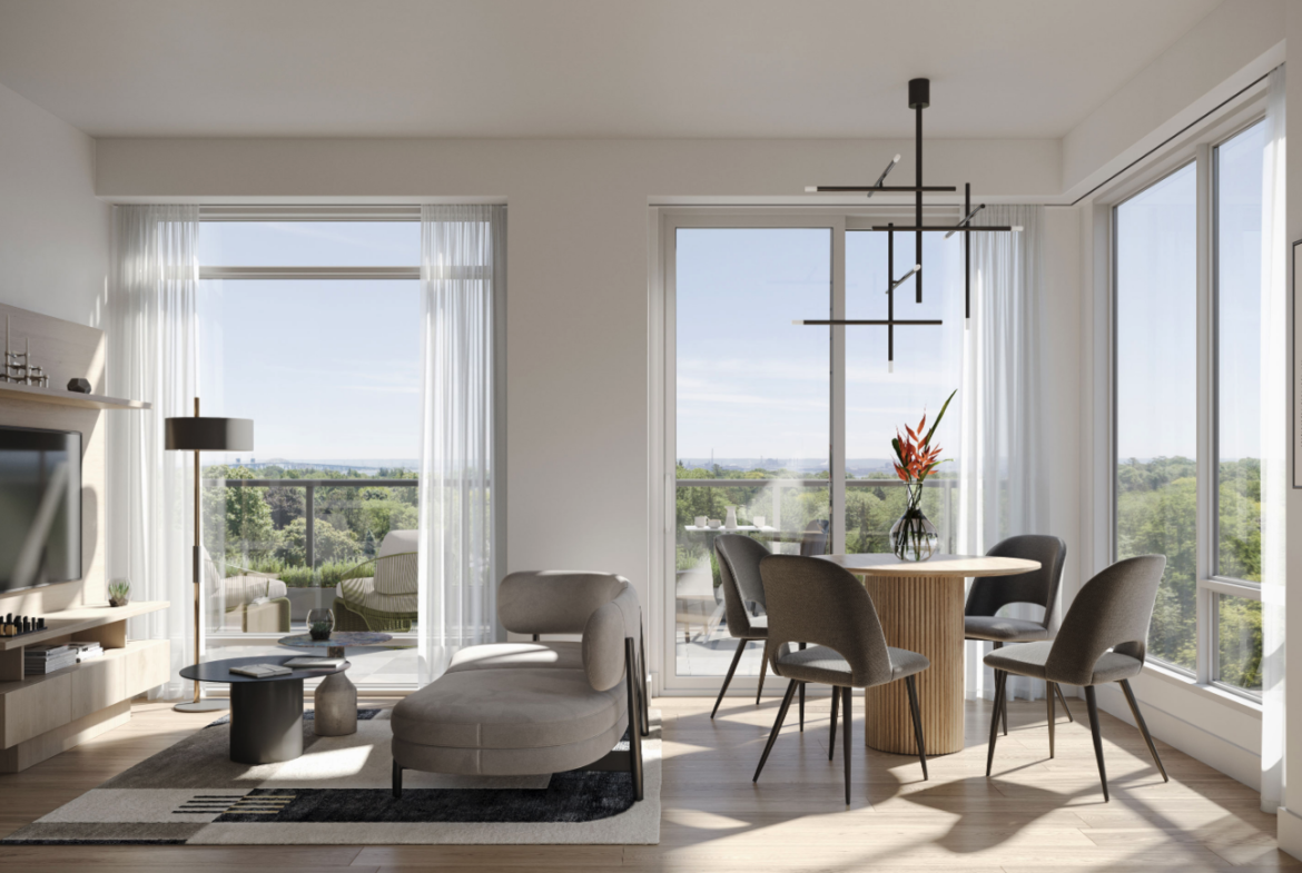 A modern living room with large windows overlooking a scenic view. The room features a cozy sofa, a small coffee table, and a round dining table with chairs. A contemporary chandelier hangs from the ceiling, and a vase with flowers decorates the table—perfect for those exploring new condos in Brampton.
