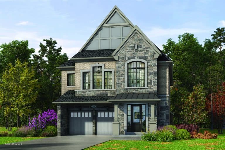 The two-story Oakridge Green Homes residence boasts a stone and brick exterior with a double garage and large windows. Its peaked roof is surrounded by trees, offering lush greenery alongside a tasteful garden of shrubs and flowers in the front yard.