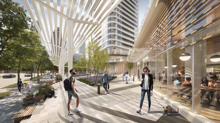 A modern urban streetscape with people walking on a sunlit plaza. High-rise buildings, including Park Place VMC Condos, and a canopy structure provide shade. Trees line the sidewalk as individuals sit, stroll, and interact in this lively, open space.