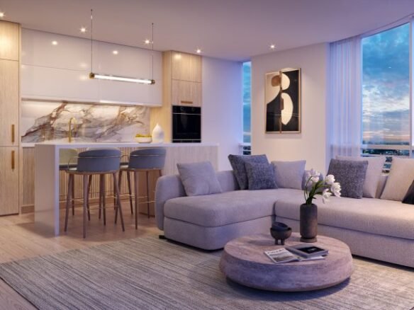 Modern apartment interior at VMC Condos features an open-plan design with a kitchen and living area. The kitchen boasts light wood cabinets, a marble backsplash, and bar stools. The living area offers a gray sectional sofa, round table, and floor lamp. Large windows provide stunning city views.