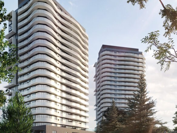 Two modern high-rise buildings with curved balconies stand under a clear sky. The structures, surrounded by trees, add a touch of greenery to this urban setting. Sunlight casts soft shadows on the facades of these new condos in Brampton, offering an impressive blend of nature and architecture.