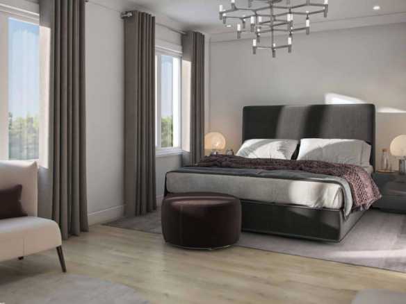 A modern bedroom in new homes features a large, dark grey upholstered bed with white and grey bedding complemented by a brown throw blanket. A stylish chandelier, round brown ottoman, cream chair, and two nightstands with lamps add elegance. Large windows with grey curtains invite natural light.