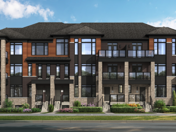 A modern townhouse building with three floors features large windows, brick and wood accents, and multiple entryways. In Brampton's new homes area, the foreground boasts a neatly landscaped garden with shrubs and flowers, set against a clear blue sky.