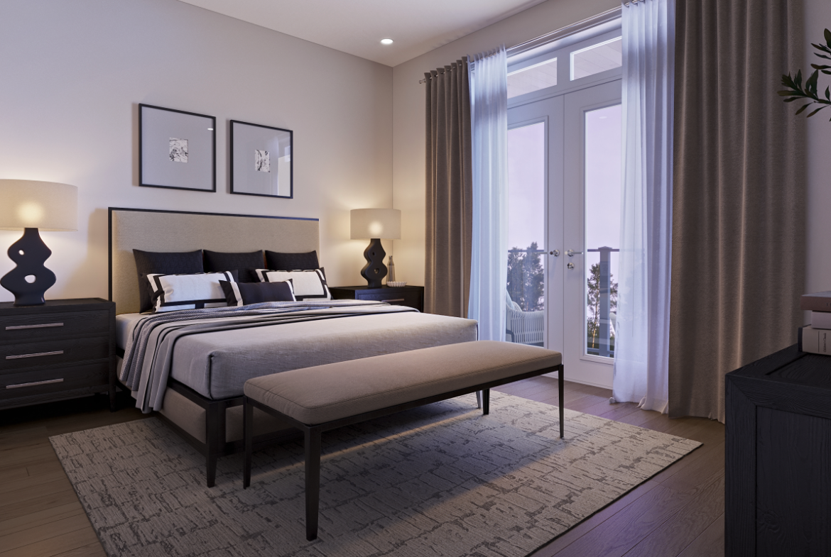 A cozy bedroom in new homes features a double bed with a gray and white striped duvet, flanked by two bedside tables with matching lamps. A bench sits at the foot of the bed, while framed art hangs above. Soft light pours through a large window with curtains, adding to the room's charm.