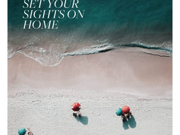 An aerial view of a sandy beach with three people under red and green umbrellas near the water's edge. Text on the image reads, "Set Your Sights on Home." Waves gently lap the shore, inviting you to dream of new homes in Toronto.