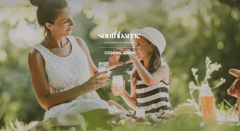 A woman and a child enjoy a picnic outdoors, holding drinks and smiling at each other. They are surrounded by greenery, with sunlight filtering through the trees. Text overlays say “South Barrie Towns” and “COMING SOON. A woman and a child enjoy a picnic outdoors, holding drinks and smiling at each other. They are surrounded by greenery, with sunlight filtering through the trees. Text overlays say "South Barrie Towns" and "COMING SOON.