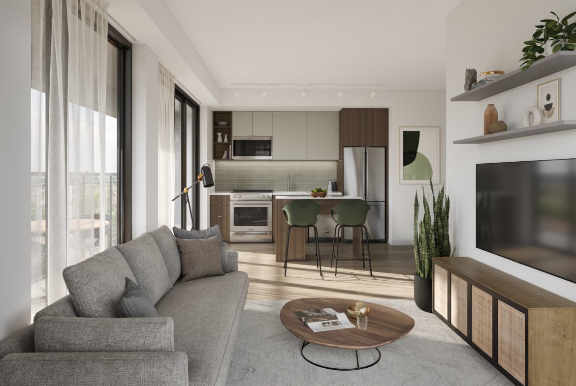 A modern living room and kitchen area with floor-to-ceiling windows in one of Toronto's new homes. It features a gray sofa, round wooden coffee table, wall-mounted TV, and a kitchen with green and brown cabinets. A plant and bar stools add accents to the space.