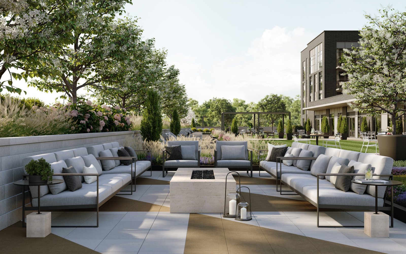 A modern outdoor patio features sleek gray sofas encircling a central rectangular stone fire pit. Adorned with potted plants and lanterns, this serene setting is enriched by the backdrop of trees and a contemporary building, ideal for new homes in Toronto.