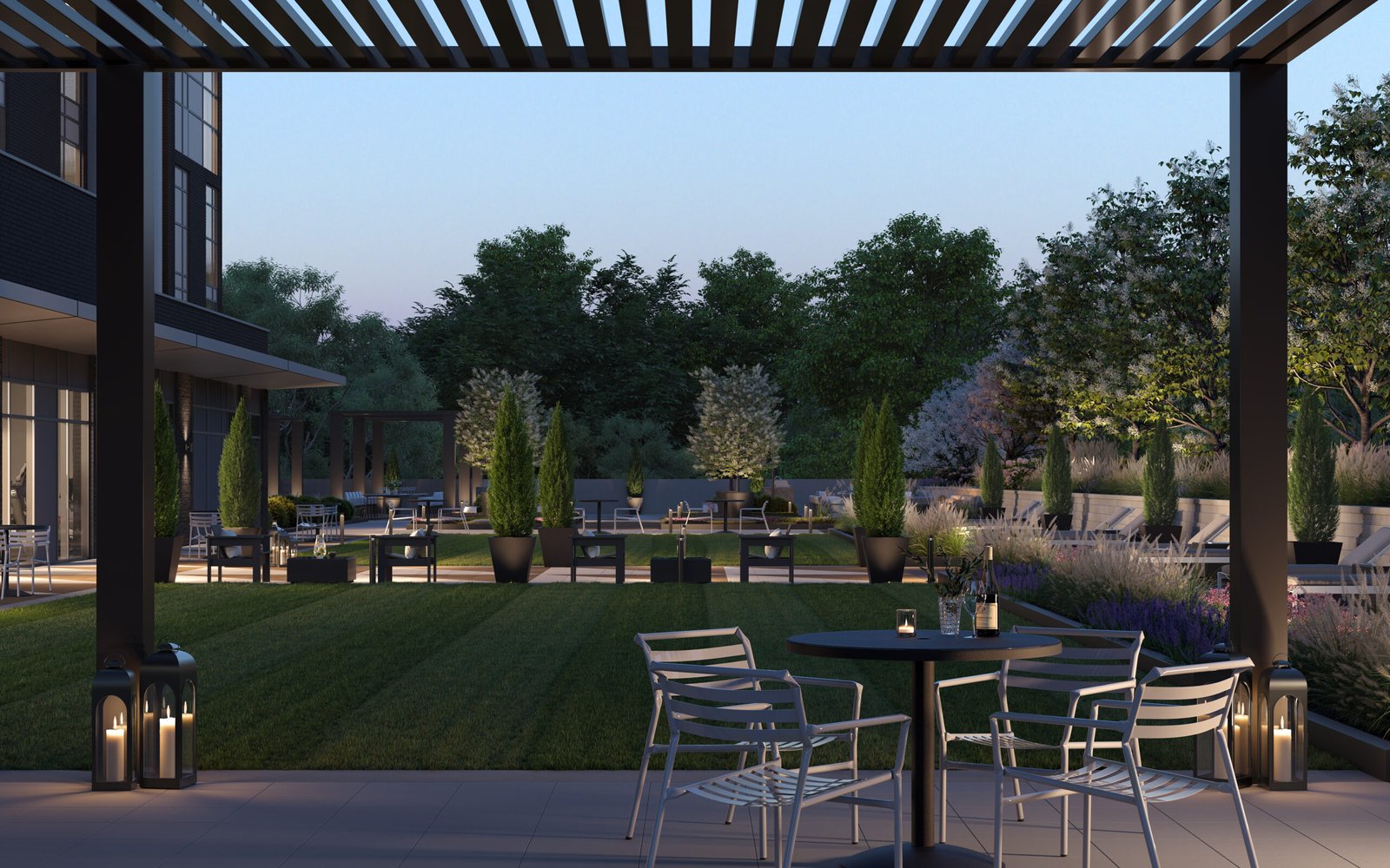 A modern outdoor patio at dusk features metal chairs and tables, embraced by lush greenery and tall potted plants. Soft lighting and lanterns add coziness. In the background, trees frame a softly lit building, hinting at the elegance of new homes.