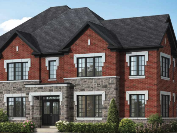 A two-story red brick house with gray stone accents and multiple windows, featuring a dark gray roof. The front yard is beautifully landscaped with small shrubs and greenery under a clear blue sky, reminiscent of the charm often found in new homes.