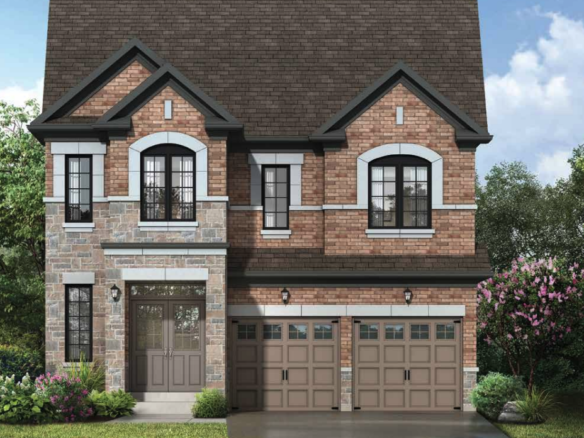 A two-story brick house with a stone facade features large windows and a brown shingled roof. This pre-construction home boasts two garage doors and is surrounded by green shrubs and trees under a clear blue sky.