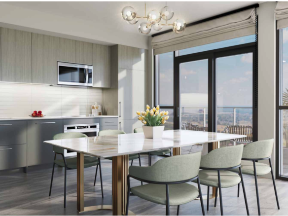 Modern kitchen and dining area in new homes feature light gray cabinets, a sleek white dining table, and pastel green chairs. Large floor-to-ceiling windows offer a scenic view. A decorative light fixture hangs above the table, with a vase of yellow tulips perfectly centered.