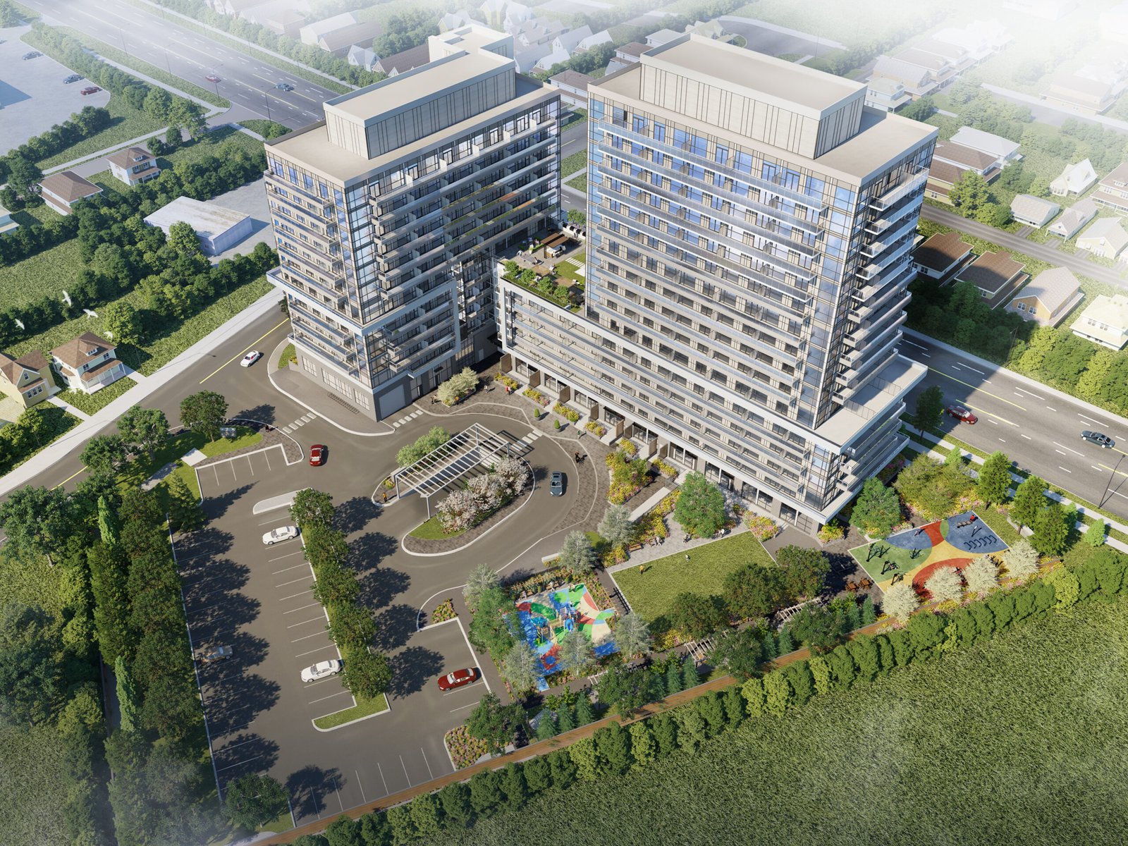 Aerial view of a modern building complex with two tall, adjacent structures and a curved entrance driveway. The area includes a playground, landscaped greenery, and a parking lot, surrounded by roads and residential houses showcasing new homes in Brampton.
