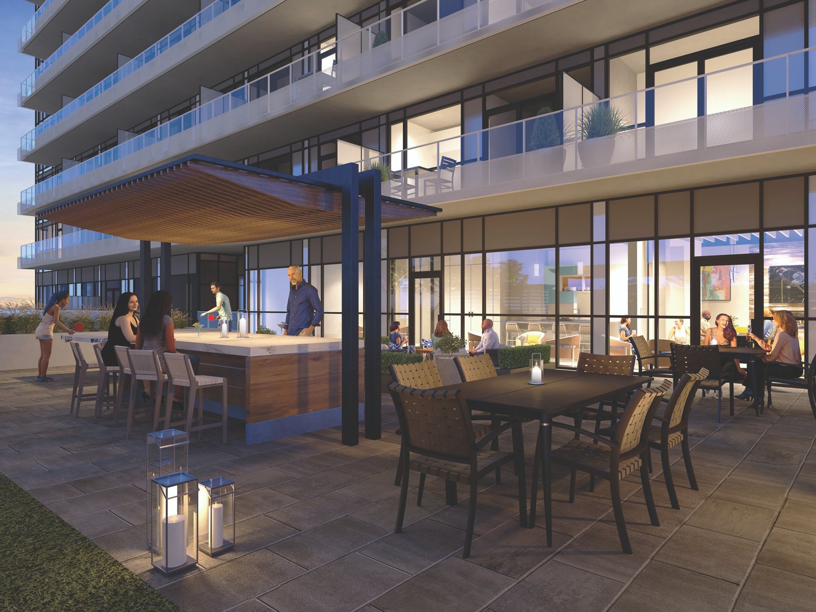 A modern outdoor patio at an apartment building with people socializing. The space features a covered bar area with stools, a dining table with chairs, and decorative lanterns. Large glass windows reveal a warmly lit interior, embodying the charm of new homes in Brampton.