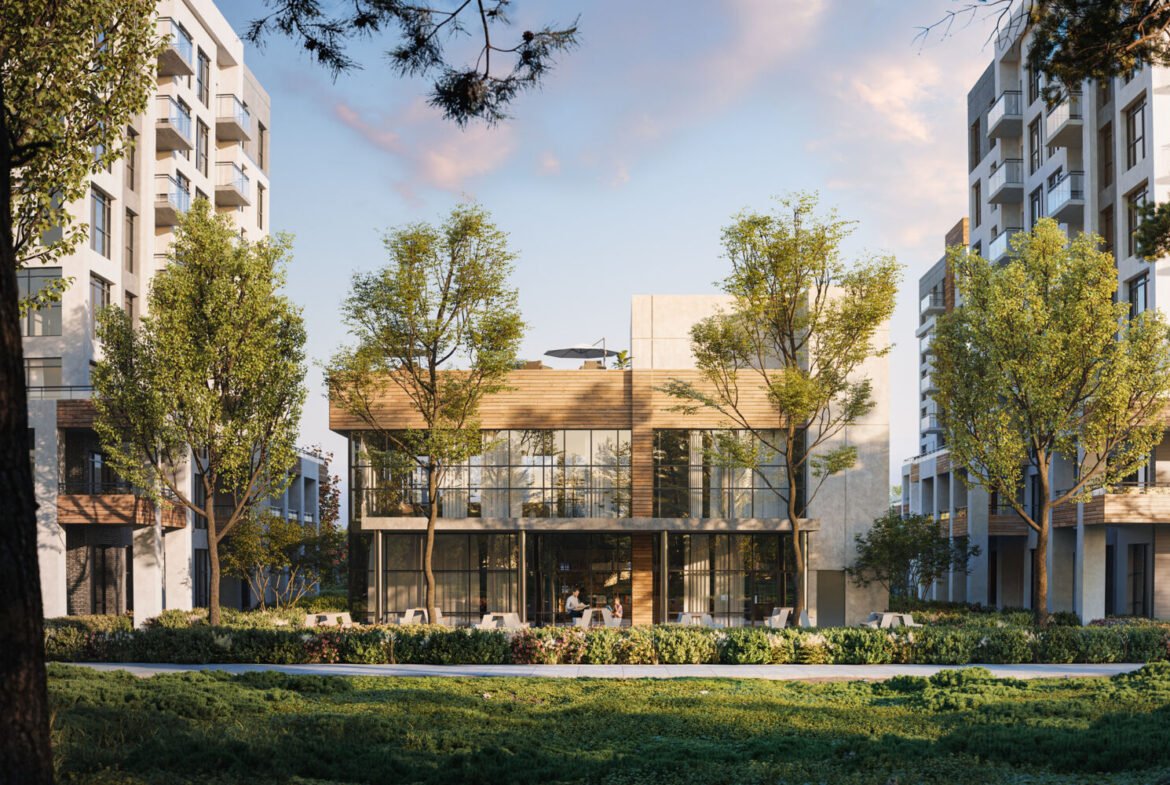 The modern, glass-fronted building, known as Mile & Creek Condos, is surrounded by lush trees and flanked by two towering residential structures. Set under a partly cloudy sky, grass and vibrant plants enhance the scenic foreground.