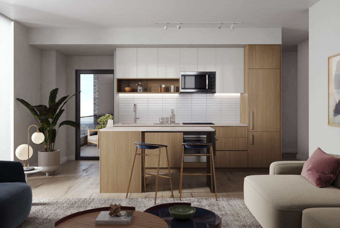 Modern kitchen with light wood cabinets and a white tile backsplash, set in one of the chic condos. Features include a central island with two bar stools and a potted plant near the glass door leading to a balcony. The cozy living area boasts a beige sofa and abstract art on the wall.