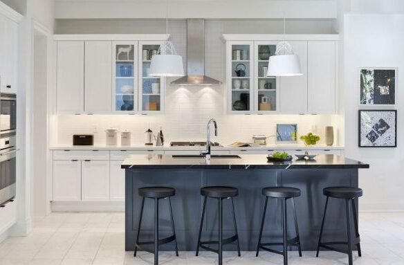 Modern kitchen in one of the new condos in GTA featuring white cabinets and a subway tile backsplash. A black island with four stools sits in the center, illuminated by pendant lights. Stainless steel appliances and framed wall art enhance the decor, while a large window provides abundant natural light.