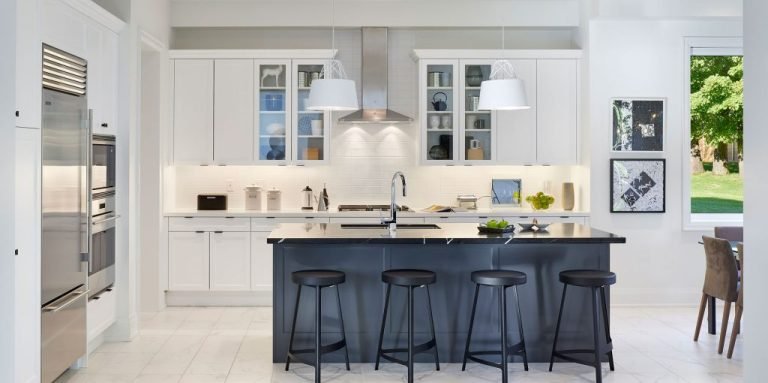 Modern kitchen in one of the new condos in GTA featuring white cabinets and a subway tile backsplash. A black island with four stools sits in the center, illuminated by pendant lights. Stainless steel appliances and framed wall art enhance the decor, while a large window provides abundant natural light.
