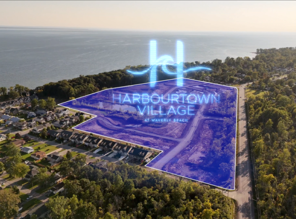 Aerial view of a coastal area with trees and houses. A translucent blue overlay highlights "Harbourtown Village at Waverly Beach," revealing new condos near the shoreline. The ocean shimmers in the background, inviting potential homeowners to explore this picturesque setting by SG Homes.