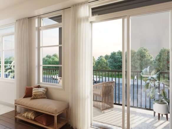 In a bright living space, sliding glass doors open to a balcony with views of green trees, typical of new homes in GTA. Inside, a cushioned bench with pillows and a potted plant by the door enhance the airy atmosphere.
