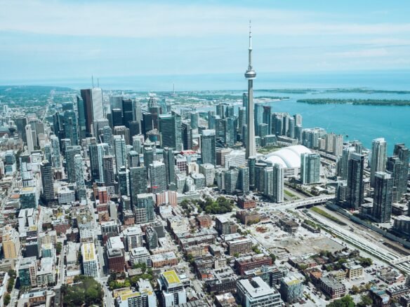 Aerial view of a bustling cityscape featuring tall skyscrapers, including new condos in GTA, with a prominent tower set against a backdrop of shimmering water and a partly cloudy sky.