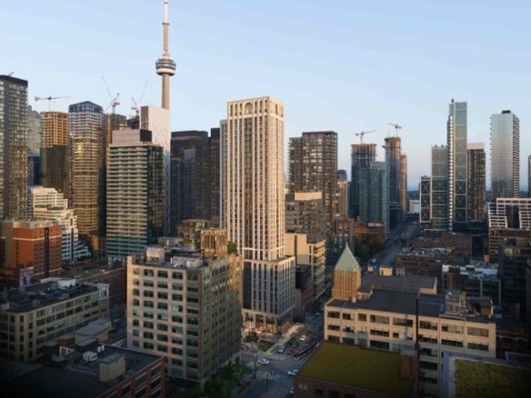 An aerial view of the city's downtown area reveals a mix of modern high-rise buildings and older structures. Prominently, a tall tower with an observation deck stands out. The cityscape is illuminated by natural daylight, with cranes indicating ongoing construction near 101 Spadina Condos.