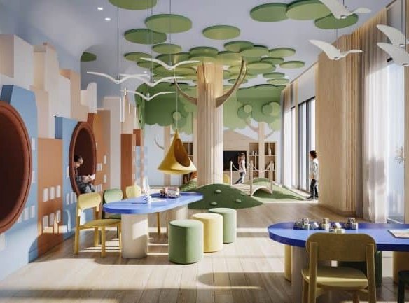 A brightly lit children's playroom with a nature theme, perfect for families in Spadina condos. The walls boast murals of trees, and the ceiling has hanging green circles simulating foliage. Play areas feature tunnels, tables, and chairs, while large windows let in natural light at 101 Spadina.