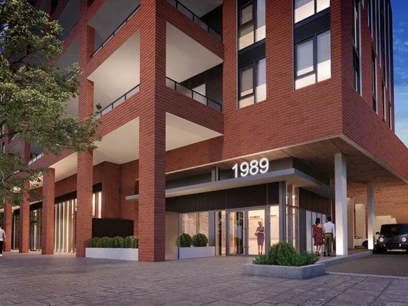 A modern multi-story brick condominium with large glass windows and balconies is illuminated at dusk. The entrance, with the number "1989" prominently displayed, features people walking and a parked black vehicle nearby. A tree is visible on the left.