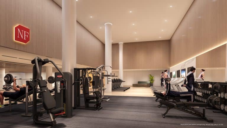 In a modern gym interior nestled within new condos, exercise machines, free weights, and treadmills buzz with activity. High ceilings and warm lighting accentuate the spaciousness, while a large wall mirror captures the energetic environment of residents dedicated to fitness.