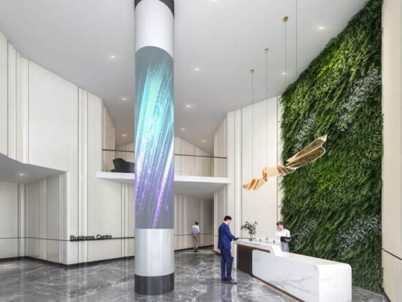 A modern office lobby with a sleek, white reception desk hosts two people interacting. A vertical LED display wraps around a column, while a green wall with plants decorates one side. The lively atmosphere is reminiscent of the innovative design found in new condos across the GTA.