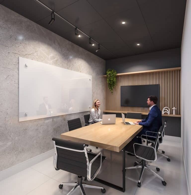 In a modern office meeting room with a long wooden table and four black chairs, two people sit with laptops facing each other. The room features a whiteboard on a textured wall and vertical plant decor. Ceiling lights illuminate the space, reminiscent of sleek designs found in new condos.