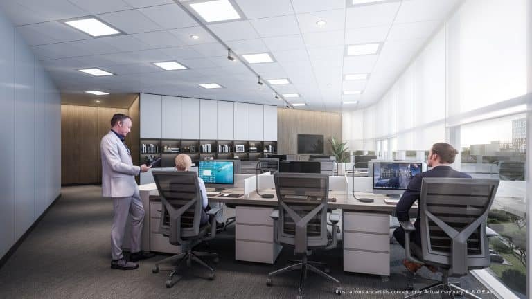 A modern office space with large windows and several workstations resembles the sleek design of new condos. Three people are seated at desks, working on computers, while another stands and talks. The room features neutral colors and contemporary furniture.