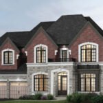 A two-story brick and stone house by Sg Homes featuring a dark roof. It has arched windows, two garage doors on the left, and a small balcony on the upper right. The surrounding landscape includes bushes and trees, beautifully illuminated with outdoor lighting.