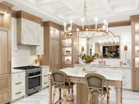 Camden Crossing A modern kitchen in Camden Crossing with light wood cabinets, a white marble countertop island, and two high-backed chairs. The space features a large circular chandelier, open shelving with decor items, a stainless steel stove, and coffered ceilings with recessed lighting.