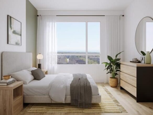 A bright, minimalist bedroom in one of the new condos boasts a large window showcasing a scenic view. It features a double bed with neutral bedding, a wooden nightstand, and a chest of drawers with a round mirror. Light wood flooring enhances the airy feel, complemented by a potted plant.