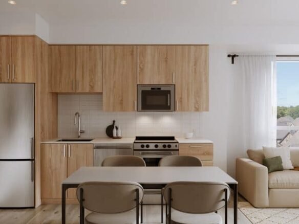 A modern kitchen in new homes in GTA features light wood cabinets, stainless steel appliances, and a white countertop. A dining table with four chairs sits nearby. To the right, a cozy living area with a beige sofa offers a bright window view, perfect for unwinding.