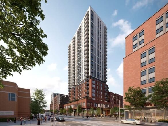A modern, tall residential building with a mix of brick and glass facade stands against a blue sky. Among the urban landscape bustling with life, it represents the new homes in GTA, surrounded by other buildings, trees, and scattered pedestrians navigating the vibrant city streets.