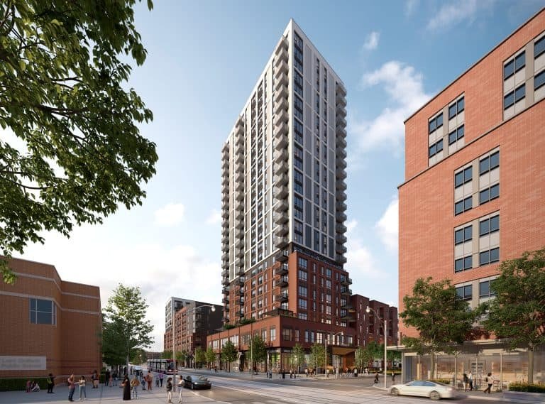A modern, tall residential building with a mix of brick and glass facade stands against a blue sky. Among the urban landscape bustling with life, it represents the new homes in GTA, surrounded by other buildings, trees, and scattered pedestrians navigating the vibrant city streets.