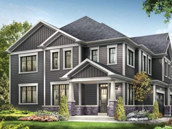 A two-story house with gray siding, white trim, and a dark gray roof stands proudly like a legacy of craftsmanship. The front entrance has a small covered porch. The yard is landscaped with green grass, colorful flowers, small bushes, and a tree. The sky above is clear and blue.