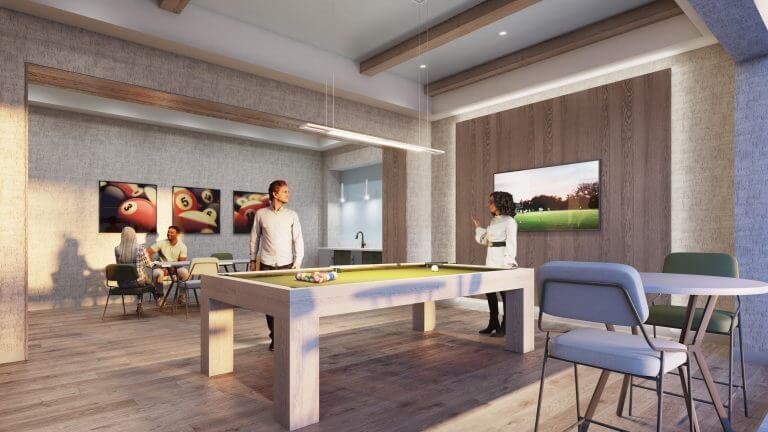 A modern recreational room in a pre-construction home features a pool table at the center. Two people are playing, while two others are seated at a table. The space boasts large windows, bright lighting, and a wall-mounted TV displaying an outdoor scene.