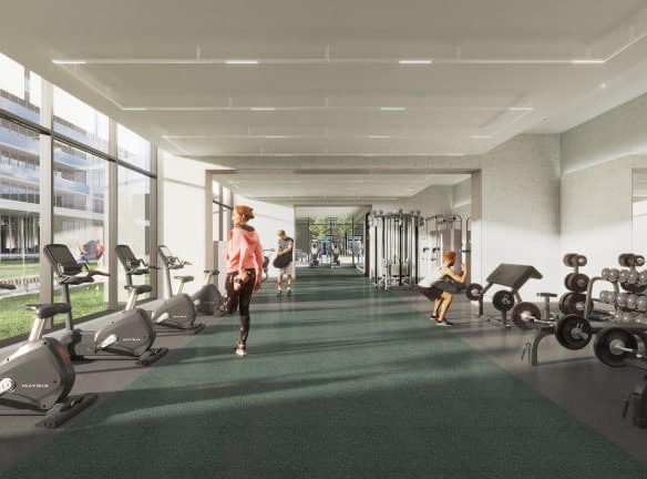 A modern gym buzzes with activity as people use exercise equipment, including stationary bikes and weight machines. Large windows offer views of the surrounding greenery, adding a touch of tranquility often sought by those exploring new homes in the GTA. Dark green carpeting complements the natural light beautifully.