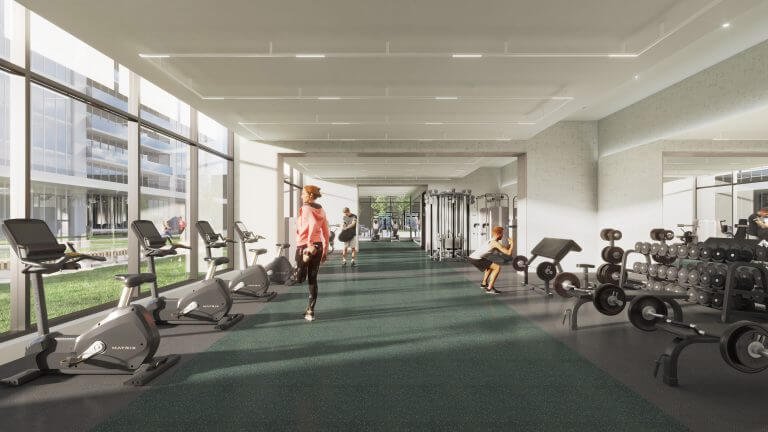 A modern gym buzzes with activity as people use exercise equipment, including stationary bikes and weight machines. Large windows offer views of the surrounding greenery, adding a touch of tranquility often sought by those exploring new homes in the GTA. Dark green carpeting complements the natural light beautifully.