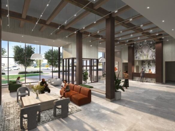 The spacious lobby of the new condos features large windows, multiple seating areas, and contemporary decor. People sit and stand engaged in conversation near a reception desk on the right. Large pendant lamps hang from the ceiling, highlighting a vibrant introduction to modern living spaces.