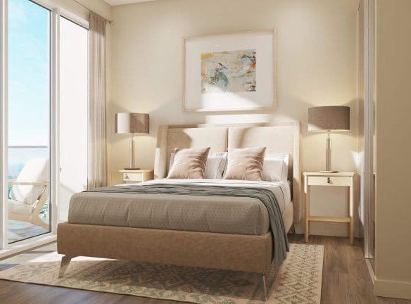 A cozy bedroom in one of the new condos features a beige bed, gray blanket, and two pillows. A large window with sheer curtains lets in natural light. Two matching lamps sit on bedside tables, and a painting hangs above the bed. A balcony with chairs is visible outside—Sg Homes living at its finest.