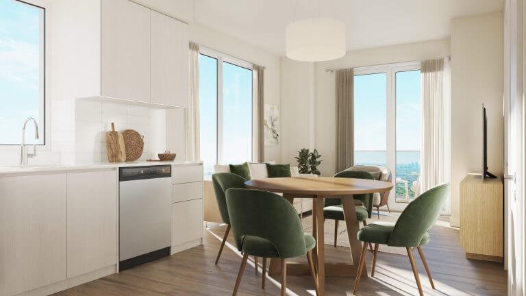 This bright, modern dining area could be yours in one of the new condos by SG Homes. Picture a round wooden table with green velvet chairs basking in sunlight streaming through large windows and a glass door, illuminating white cabinetry and wooden floors while a potted plant sits elegantly in the corner.