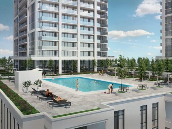 A modern residential complex, featuring new condos, boasts two tall buildings and a central outdoor swimming pool. Residents unwind on lounge chairs or stroll around the pool, enveloped by lush greenery. The sky is mostly clear with a few clouds.