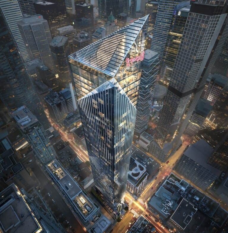 Aerial view of a modern cityscape featuring a tall, geometric skyscraper with a distinct angular design. The building is illuminated against the backdrop of neighboring high-rises and city streets lined with vehicles. Near the top, the sign reading "Freed Hotel" is visible among sleek residences.