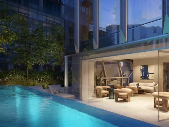 A luxurious modern indoor space at Freed Hotel & Residences boasts floor-to-ceiling windows next to a well-lit outdoor swimming pool. The sleek interior features beige furniture in a comfortable seating area and large glass doors leading to the serene, inviting pool area.