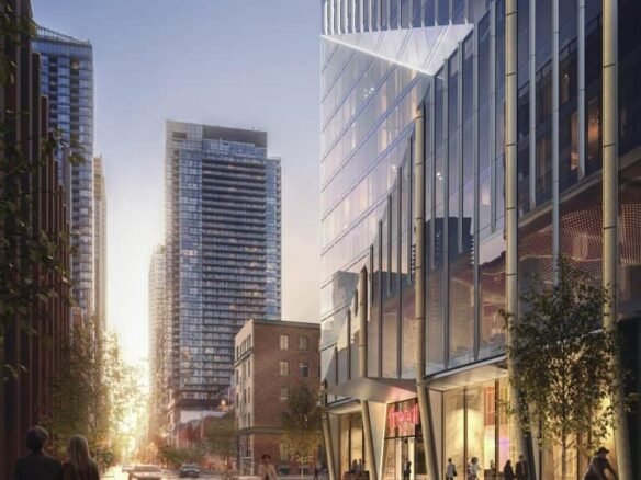 A bustling urban street at dusk, with modern high-rise buildings lining both sides. People walk along the sidewalks and a few cars drive down the road. The street is illuminated by city lights, including those from the nearby Freed Hotel Residences, and the setting sun in the background creates a warm glow.